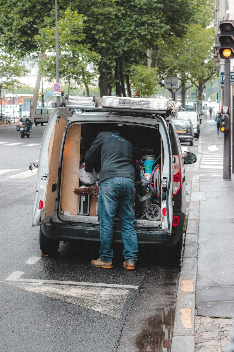 man in blue denim jeans and blue denim jeans standing on white van during daytime